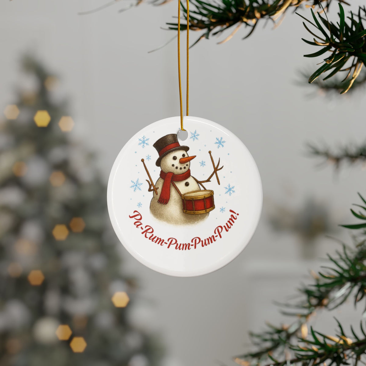 Round Christmas ornament with a snowman playing drums and snowflakes, hanging from a tree.