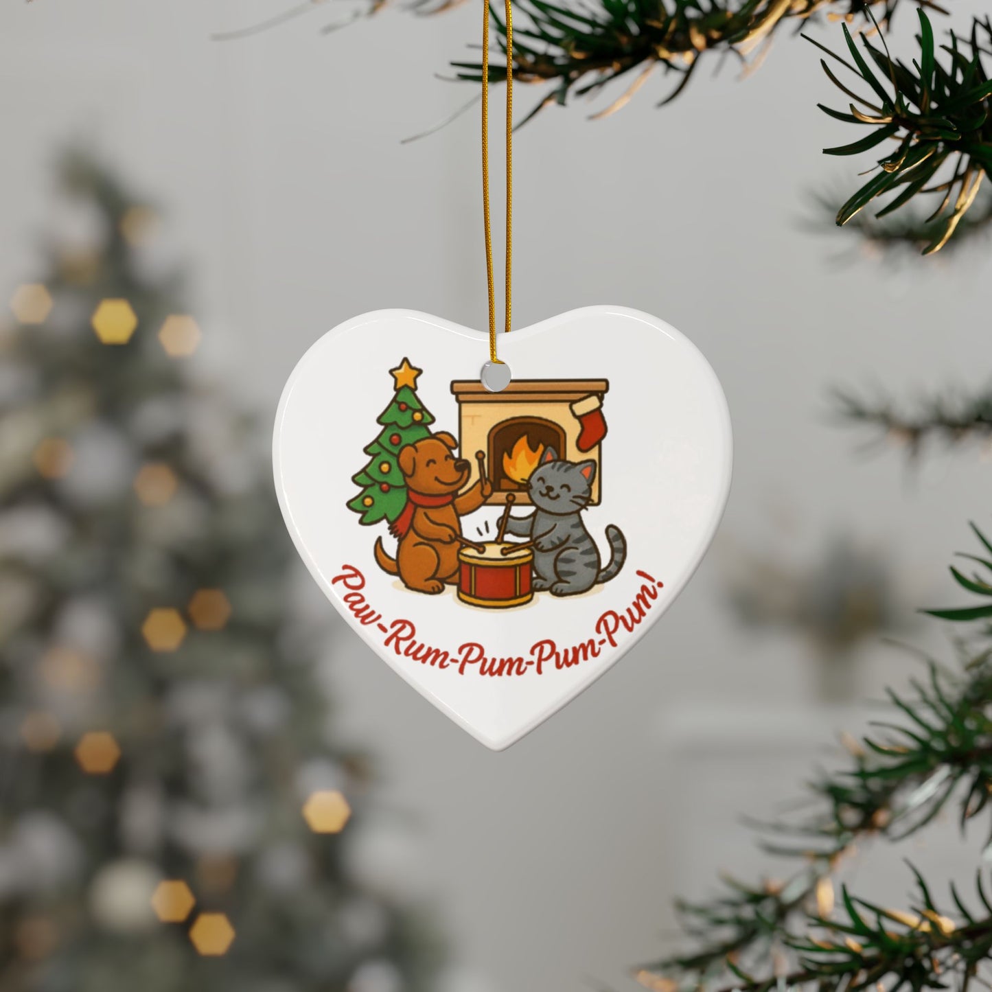 Heart-shaped Christmas ornament with cartoon dogs and a cat by a fireplace, hanging from a tree.
