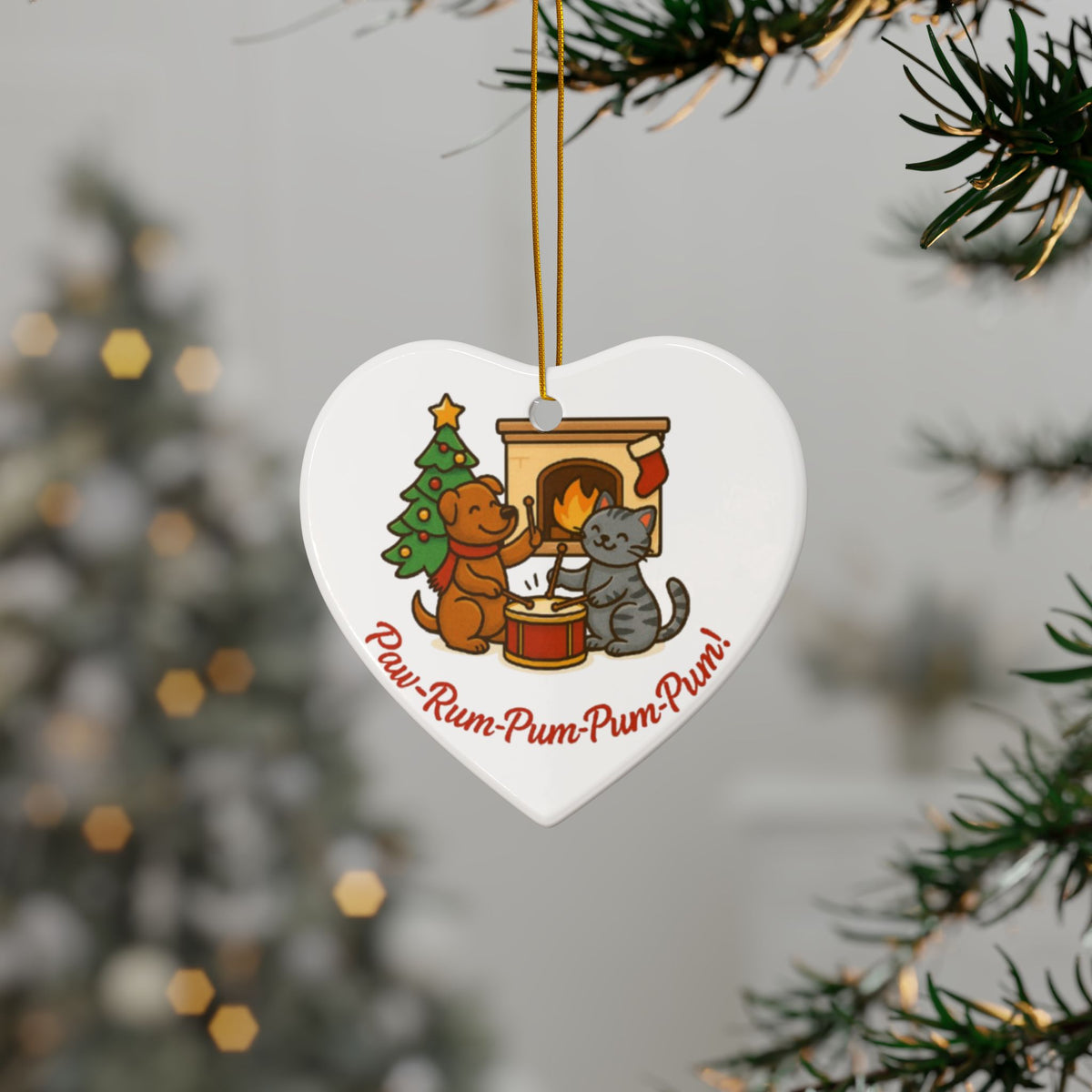 Heart-shaped Christmas ornament with cartoon dogs and a cat by a fireplace, hanging from a tree.