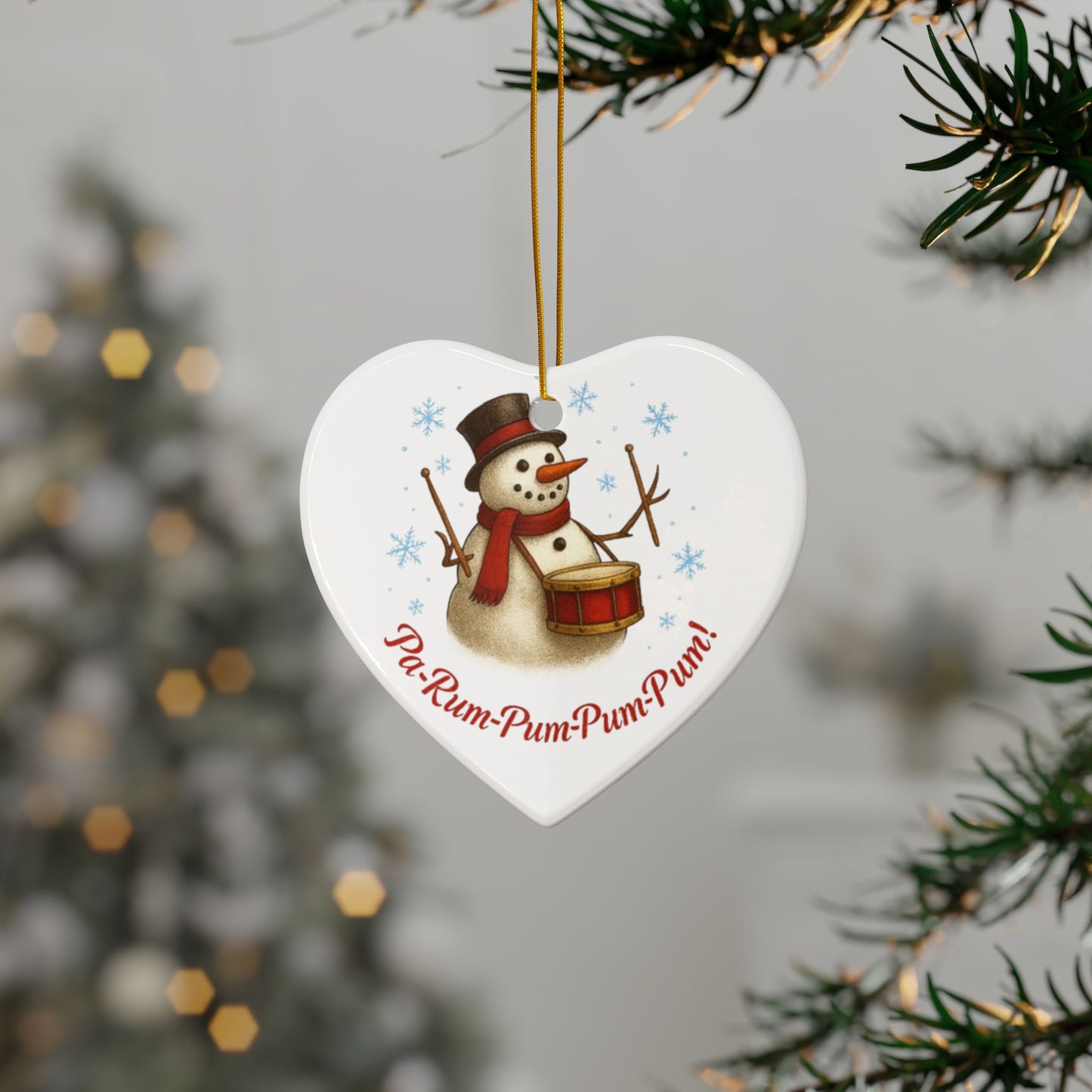 Heart-shaped Christmas ornament with a snowman design and text, hanging from a tree.