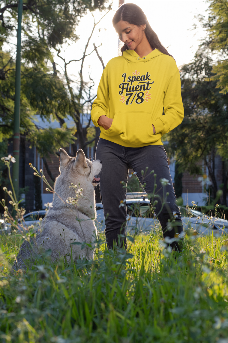Woman in a yellow hoodie with text standing next to a dog in a park